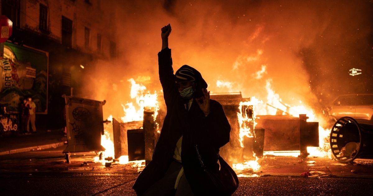 SEATTLE, WA - JUNE 08: A demonstrator raises their fist as a fire burns in the street after clashes with law enforcement near the Seattle Police Departments East Precinct shortly after midnight on June 8, 2020 in Seattle, Washington. Earlier in the evening, a suspect drove into the crowd of protesters and shot one person, which happened after a day of peaceful protests across the city. Later, police and protesters clashed violently during ongoing Black Lives Matter demonstrations following the death of George Floyd.