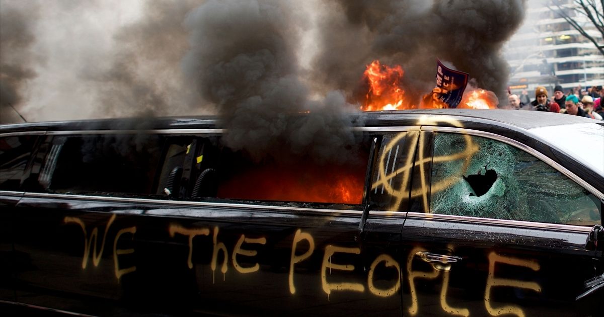 WASHINGTON, DC - JANUARY 20: A limousine is set aflame with the graffiti of "We the People" spray painted on the side after the inauguration of Donald Trump as the 45th President of the United States January 20, 2017 in Washington D.C. Hundreds of thousands of people combined to celebrate and protest.