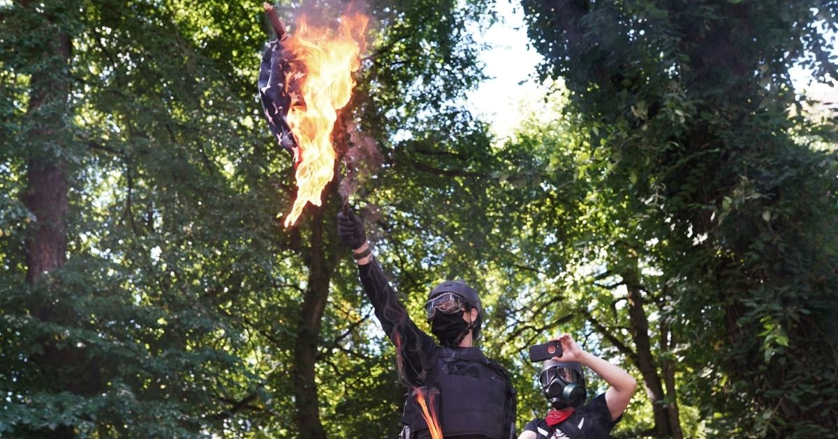 PORTLAND, OR - AUGUST 22: Anti-police protesters burn an American flag while facing off with right wing groups in front of the Multnomah County Justice Center on August 22, 2020 in Portland, Oregon. For the second Saturday in a row, right wing groups gathered in downtown Portland, sparking counter protests and violence.