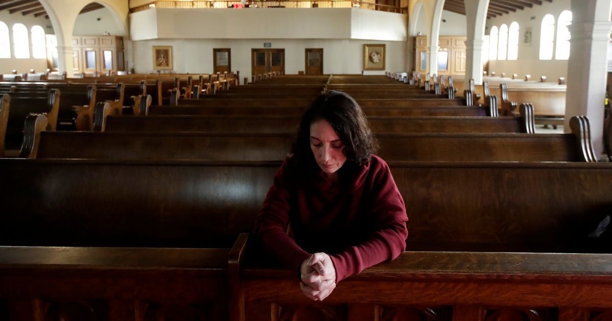 A woman listens as the Rev. Roger Gustafson is recorded celebrating Mass in an empty St. Brendan the Navigator Catholic Church in San Francisco on March 28, 2020.