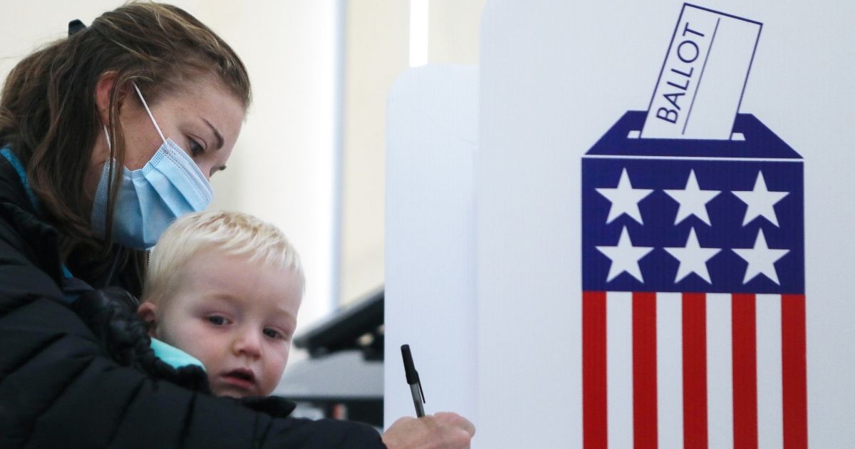 A voter holds a child as she fills out her ballot during early voting in the presidential election Thursday in Adel, Iowa.