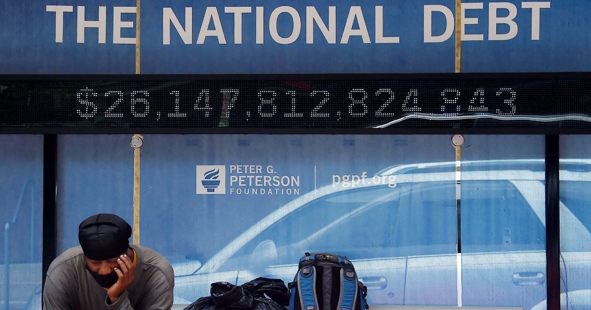 A man waits at a bus stop that displays the national debt of the United States on June 19, 2020, in Washington, D.C.