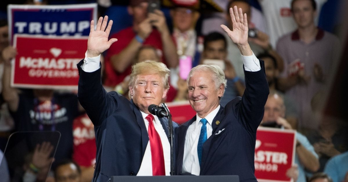 President Donald Trump and South Carolina Gov. Henry McMaster raise their arms during a campaign event at Airport High School in West Columbia, South Carolina, on June 25, 2018.