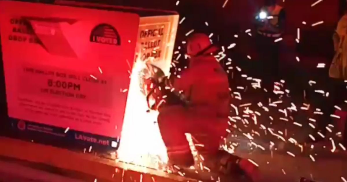 A firefighter in Baldwin Park, California, cuts into a ballot box that was on fire in order to extinguish the blaze with water from a fire hose on Oct. 18, 2020.