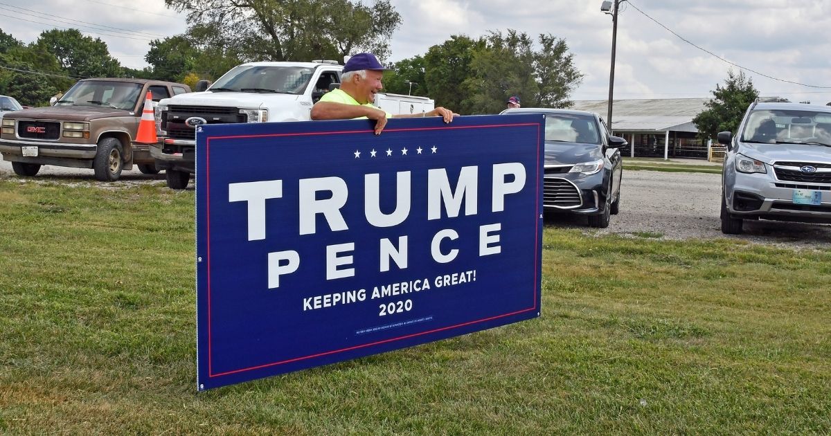 A Kansas man poses with a "Trump/Pence 2020" sign.