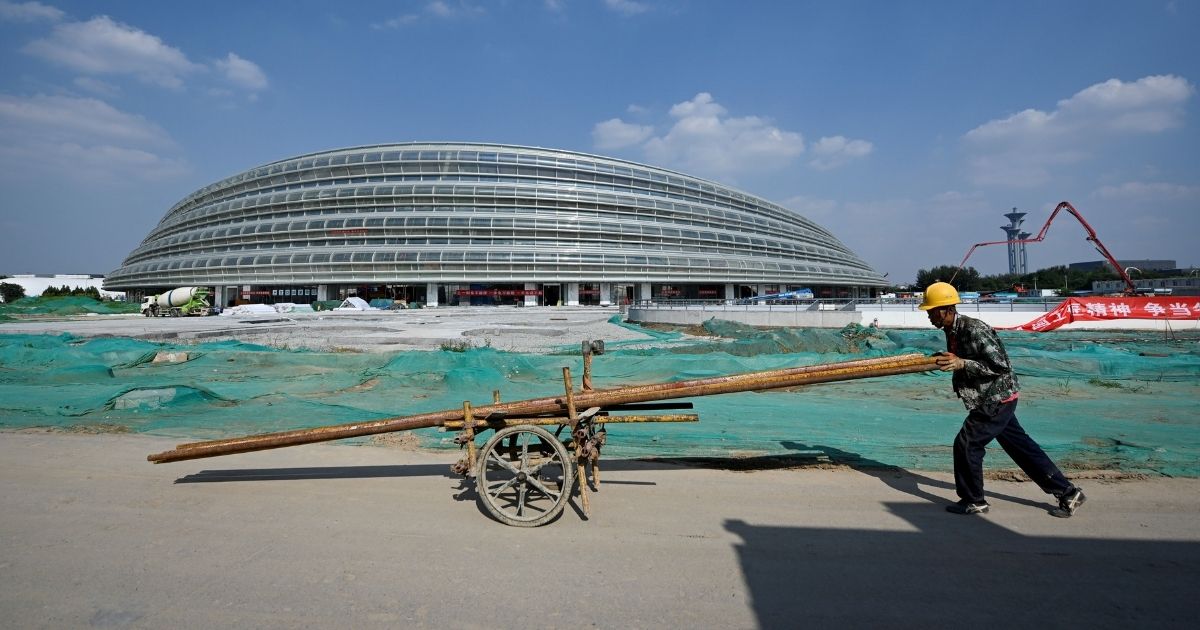 A worker pushes a wheelbarrow in front of the National Speed Skating Oval, the venue being built for speed skating events at the 2022 Winter Olympics, in Beijing on Aug. 21, 2020.