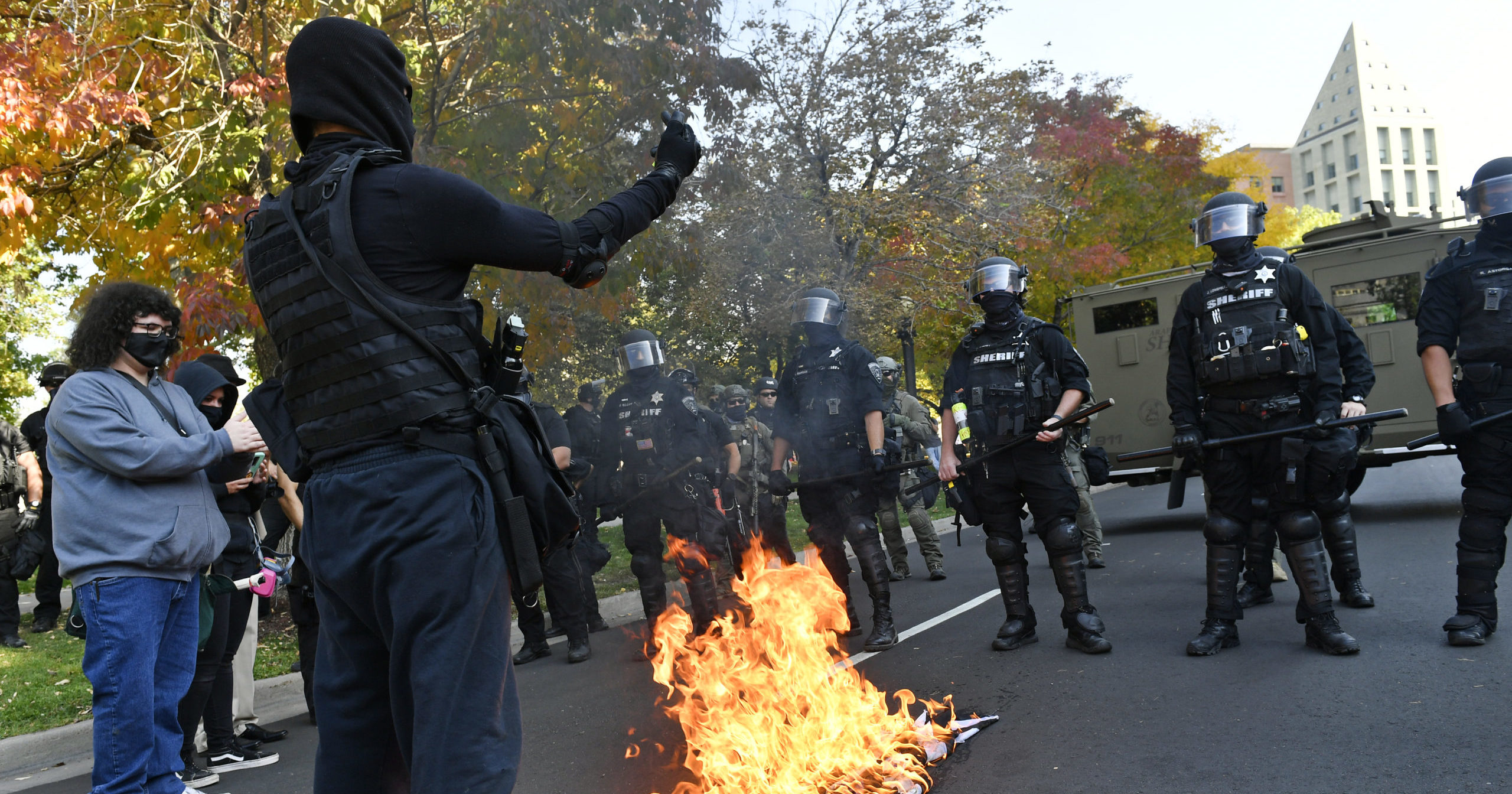 Protesters burn a police flag in front of law enforcement officers during dueling rallies between right- and left-wing groups on Oct. 10, 2020, in Denver.