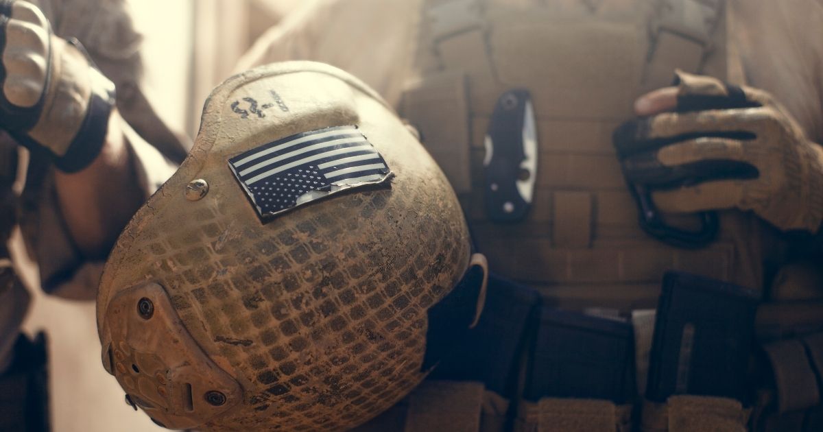 A soldier carries his helmet in the above stock image.