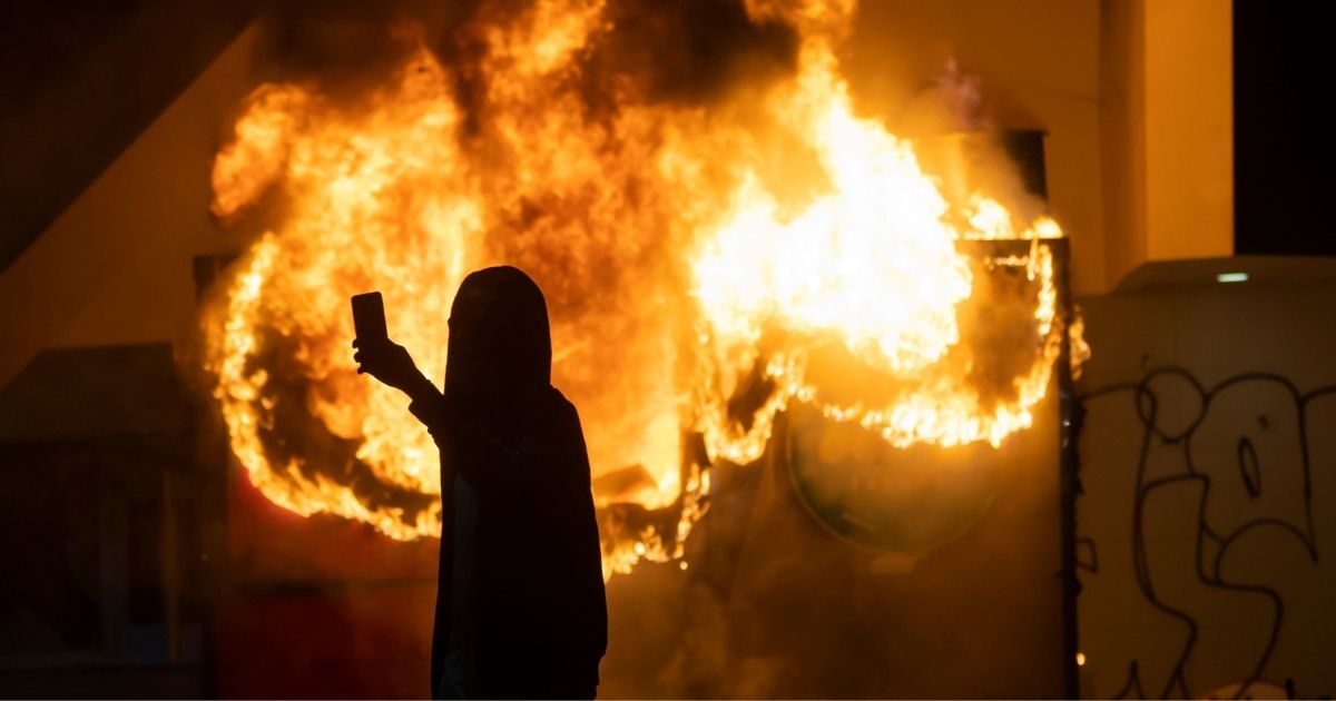 A protester takes a selfie in front of a burning building.