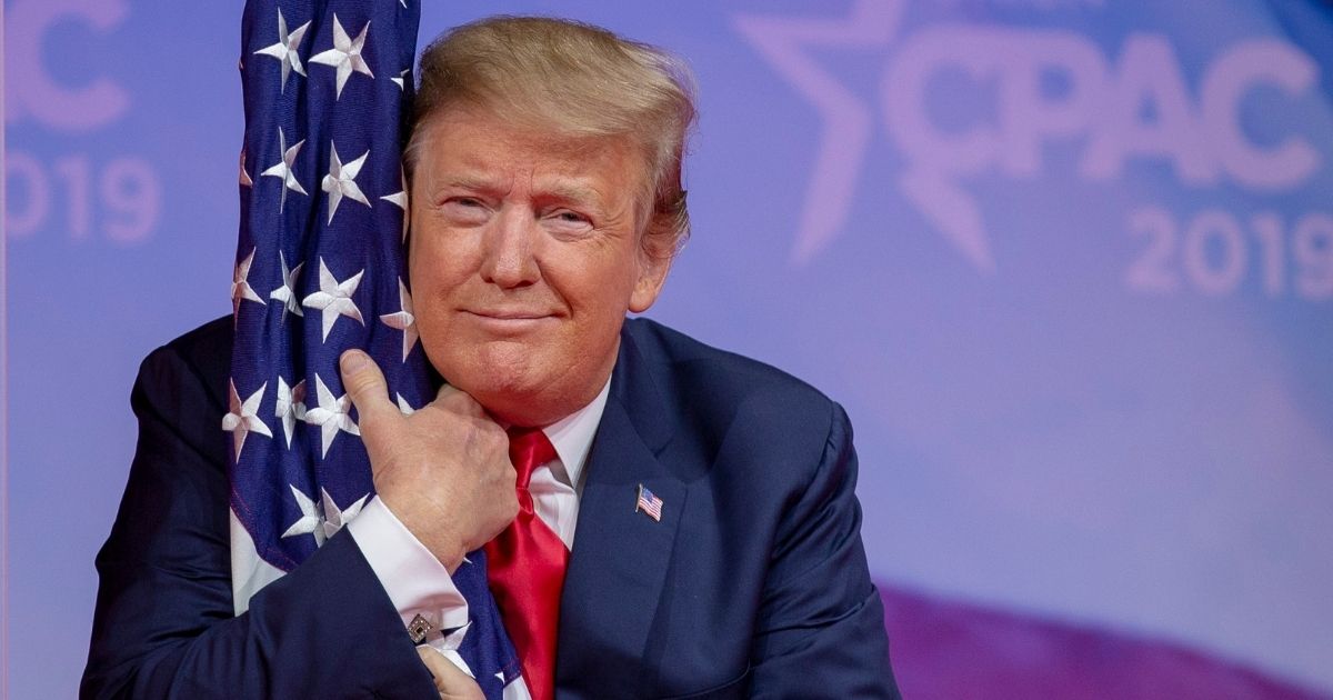 President Donald Trump hugs the U.S. flag during CPAC 2019 on March 2, 2019, in National Harbor, Maryland.