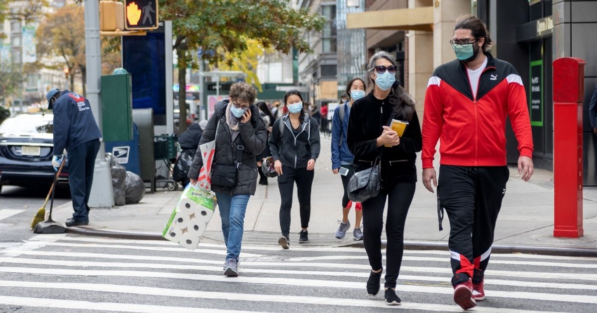 People wearing masks walk through a crosswalk on Saturday in New York City.