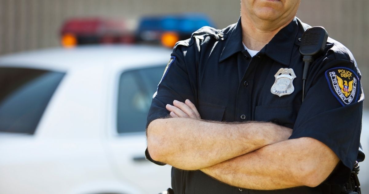 The stock photo above shows a police officer standing by a car.