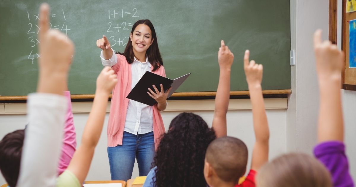 A teacher asks her elementary school students a question in the stock image above.