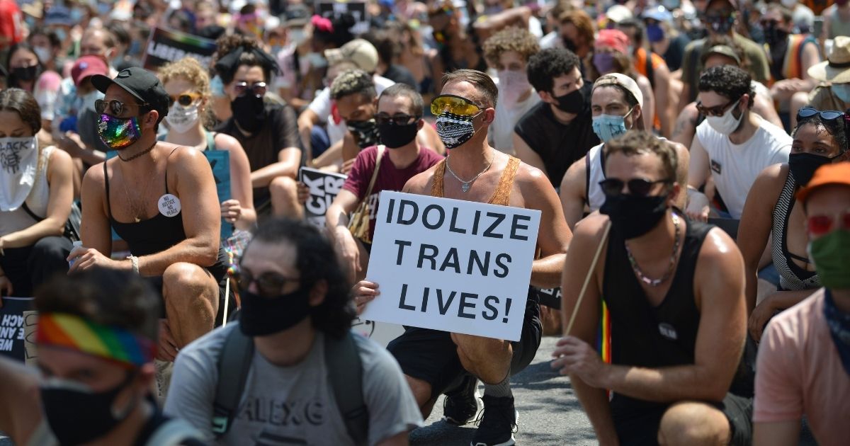 A person taking a knee with others holds an 'Idolize Trans Lives' sign at the Queer Liberation March for Black Lives & Against Police Brutality on June 28, 2020, in New York City.