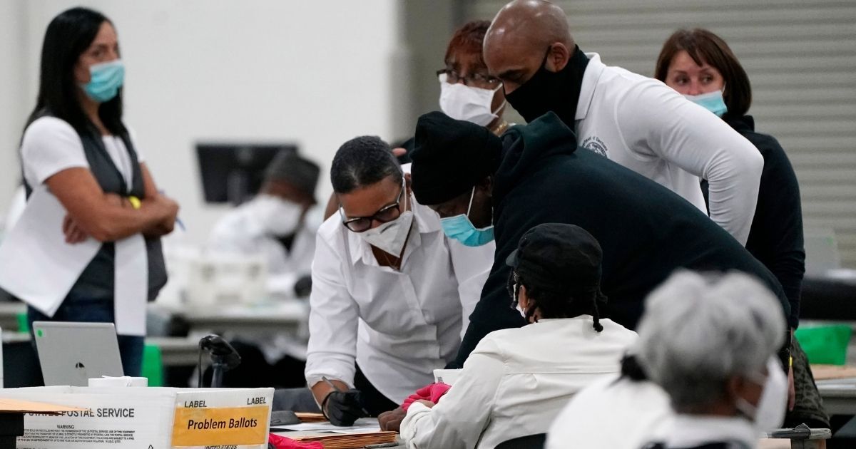 Election officials huddle around a table as absentee ballots are processed at the central counting board on Nov. 4, 2020, in Detroit.