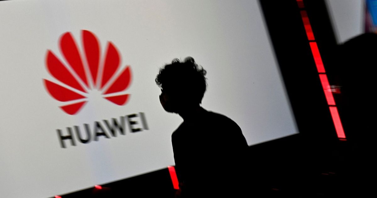 A visitor with a face mask walks past the Huawei logo displayed on a screen during an international trade show for consumer electronics and home appliances in Berlin on Sept. 3, 2020.