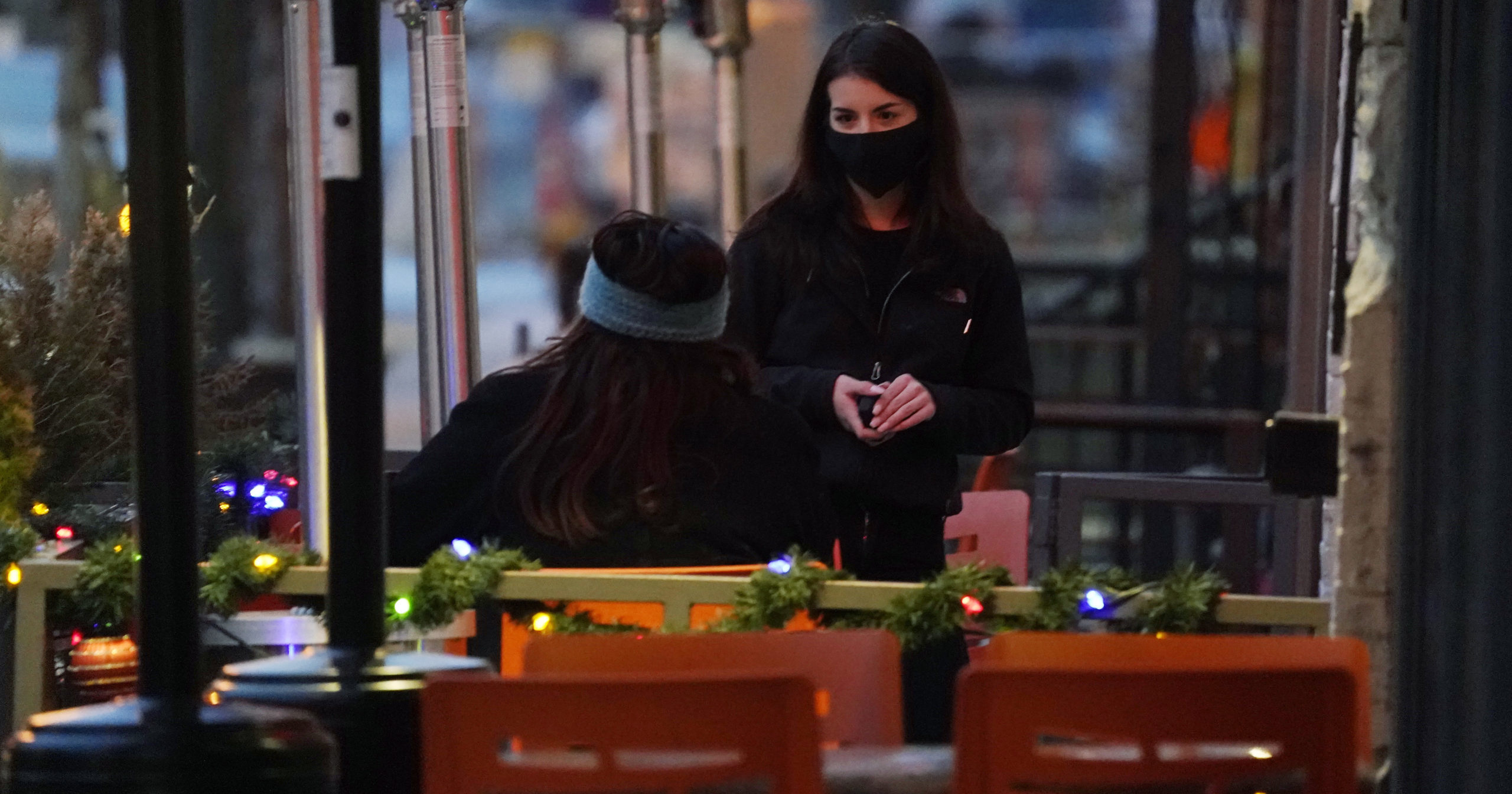 A waitperson wears a face mask while tending to a patron sitting in the outdoor patio of a sushi restaurant on Dec. 28, 2020, in downtown Denver.