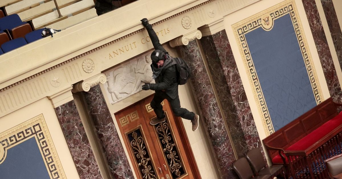 A rioter is seen hanging from the balcony in the Senate Chamber after the Capitol was taken over Wednesday.