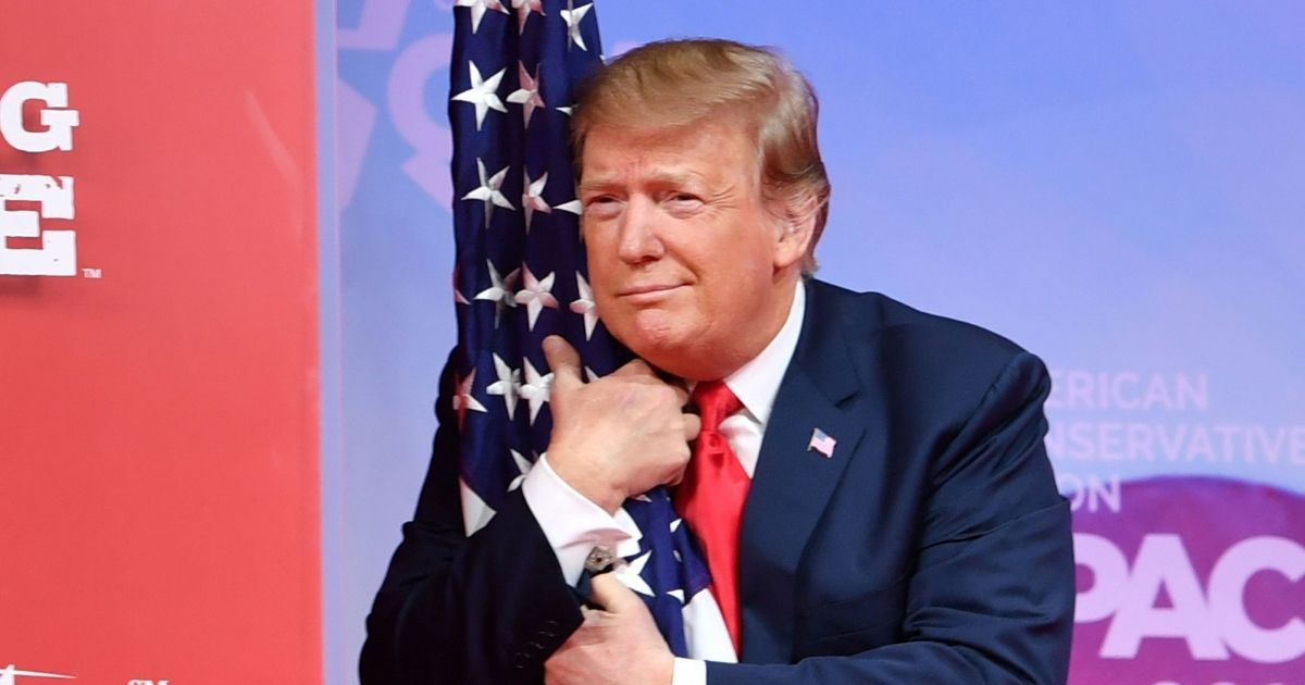 President Donald Trump hugs the U.S. flag as he arrives to speak at the annual Conservative Political Action Conference in National Harbor, Maryland, on March 2, 2019.