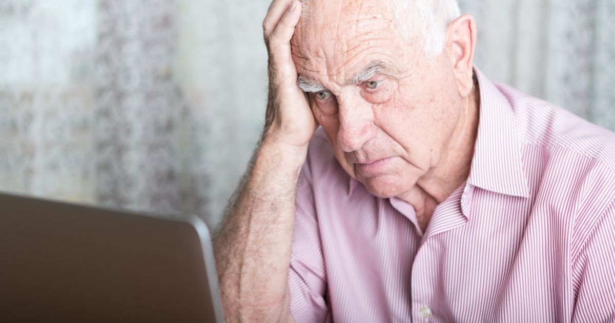 An old man looks at a computer screen with concern.