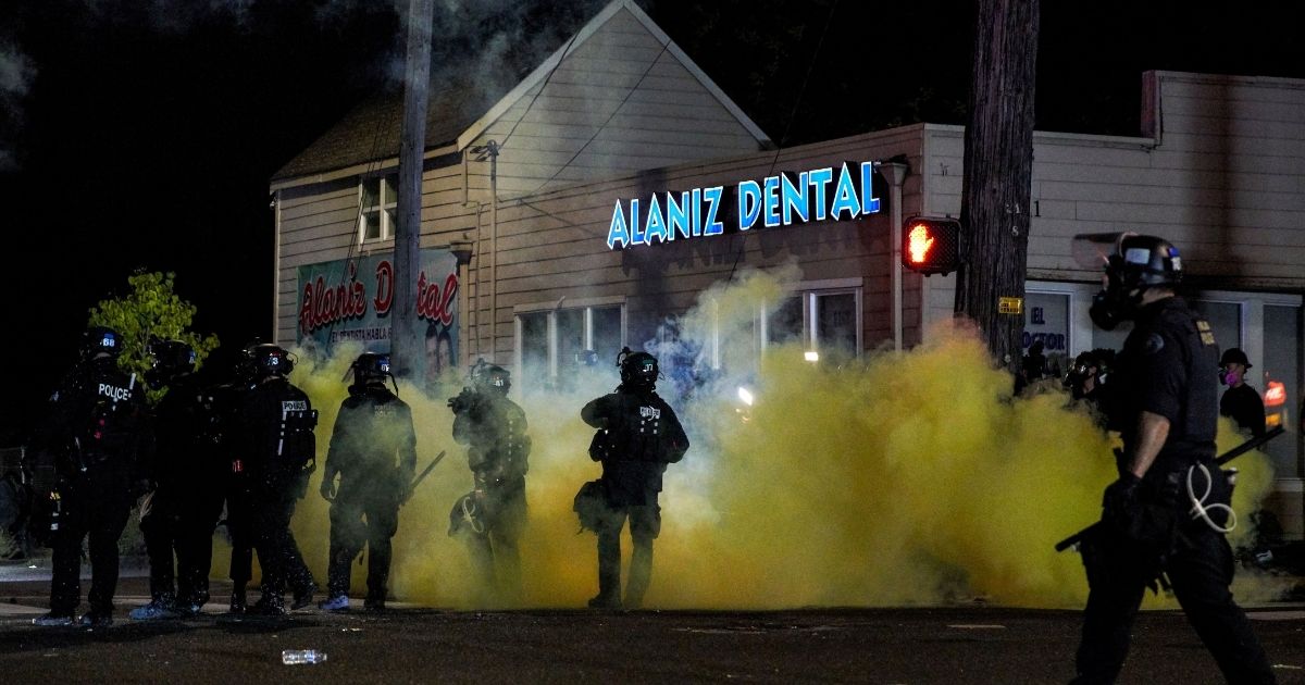 Oregon police wearing anti-riot gear march toward protesters through yellow smoke during the 100th day and night of protests in Portland, Oregon, on Sept. 5, 2020.