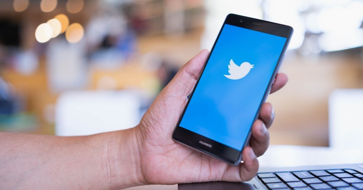 A man holding a phone displaying the Twitter logo is pictured in the stock image above.