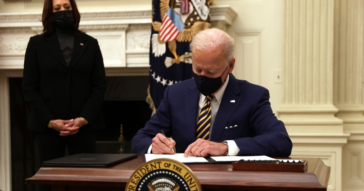 President Joe Biden signs an executive order as Vice President Kamala Harris looks on during an event on economic crisis in the State Dining Room of the White House on Jan. 22, 2021.