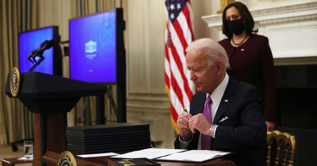 President Joe Biden signs executive orders as Vice President Kamala Harris looks on in the State Dining Room of the White House on Thursday.