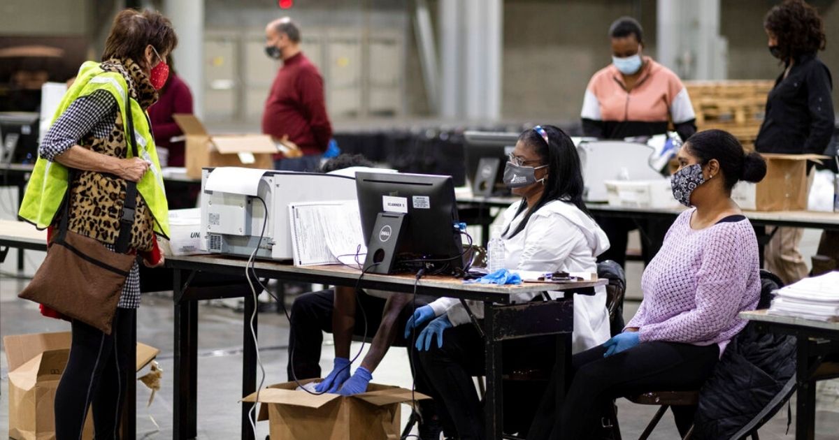 A GOP observer, left, watches as workers scan ballots as the Fulton County presidential recount gets under way Nov. 25, 2020, at the Georgia World Congress Center in Atlanta.