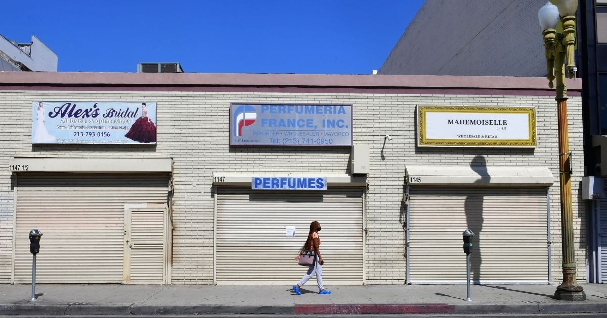 A woman walks past closed shopfronts in what would be a normally busy fashion district in Los Angeles, California on May 4, 2020.