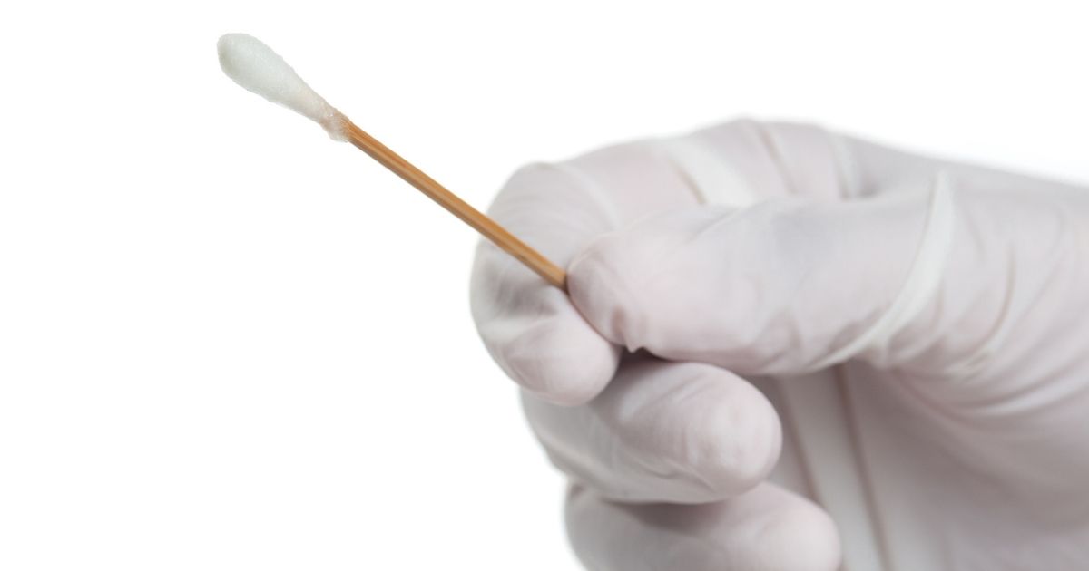 A hand with a medical glove holds a cotton swab.