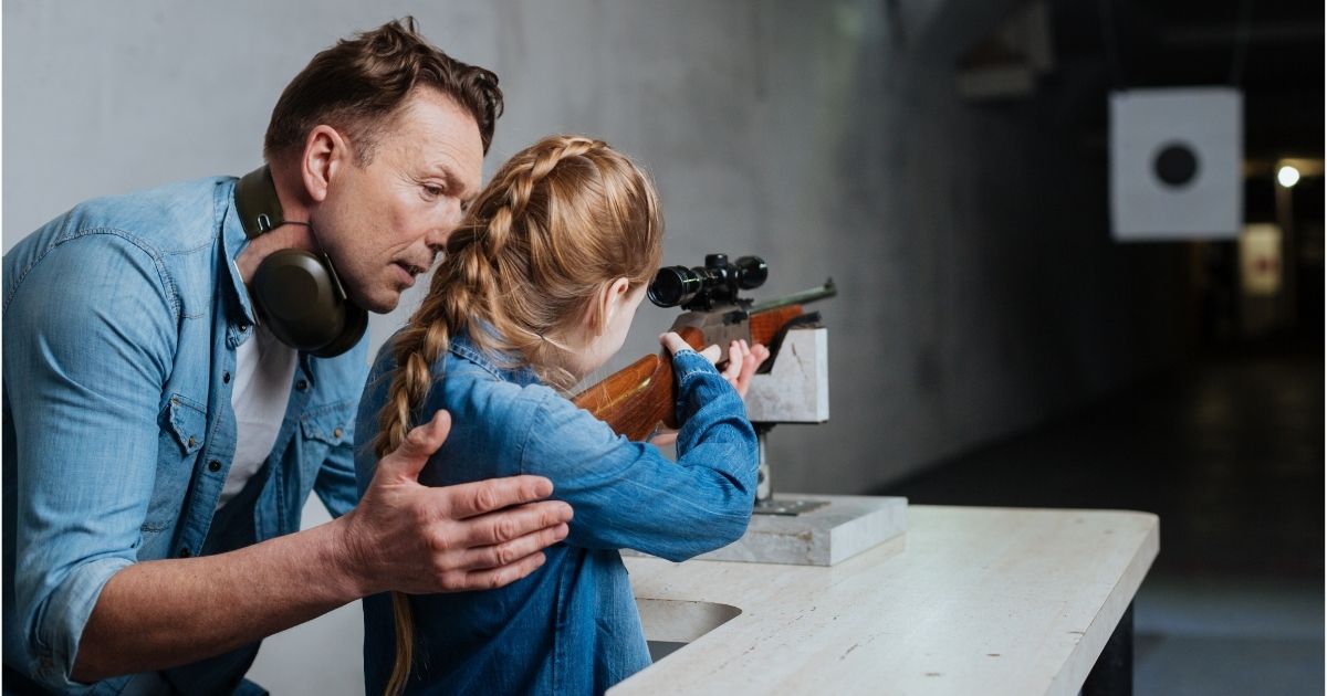 This stock photo shows a father teaching his young daughter how to shoot a gun at an instruction facility.