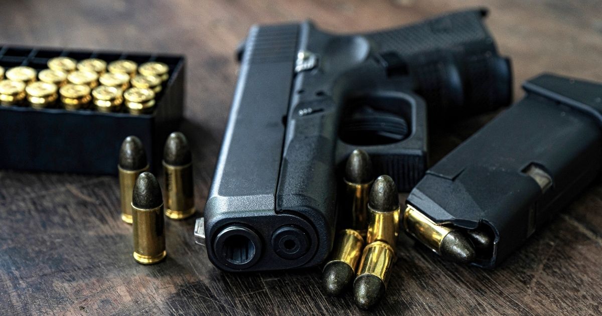 A handgun and ammunition are pictured on a wooden table in the stock image above.