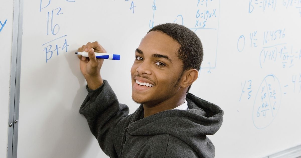 A student solves math equations on a whiteboard in the stock image above.