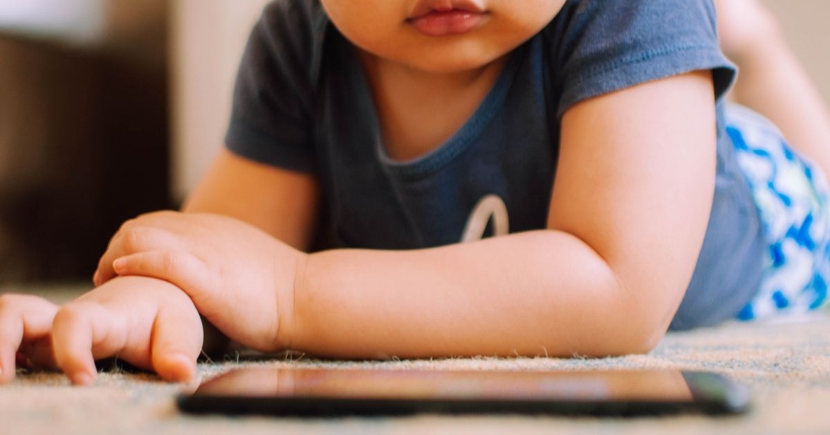 In this stock photo, a toddler watches videos on a smartphone on the floor. In Spring Hill, Florida, a toddler saved his father's life on Feb. 23, 2021, by accidentally dialing 911 on a cellphone while his father was unconscious.