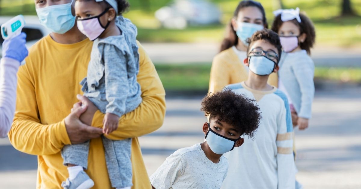A large family with four children waiting in line at a temperature checkpoint in this stock image.