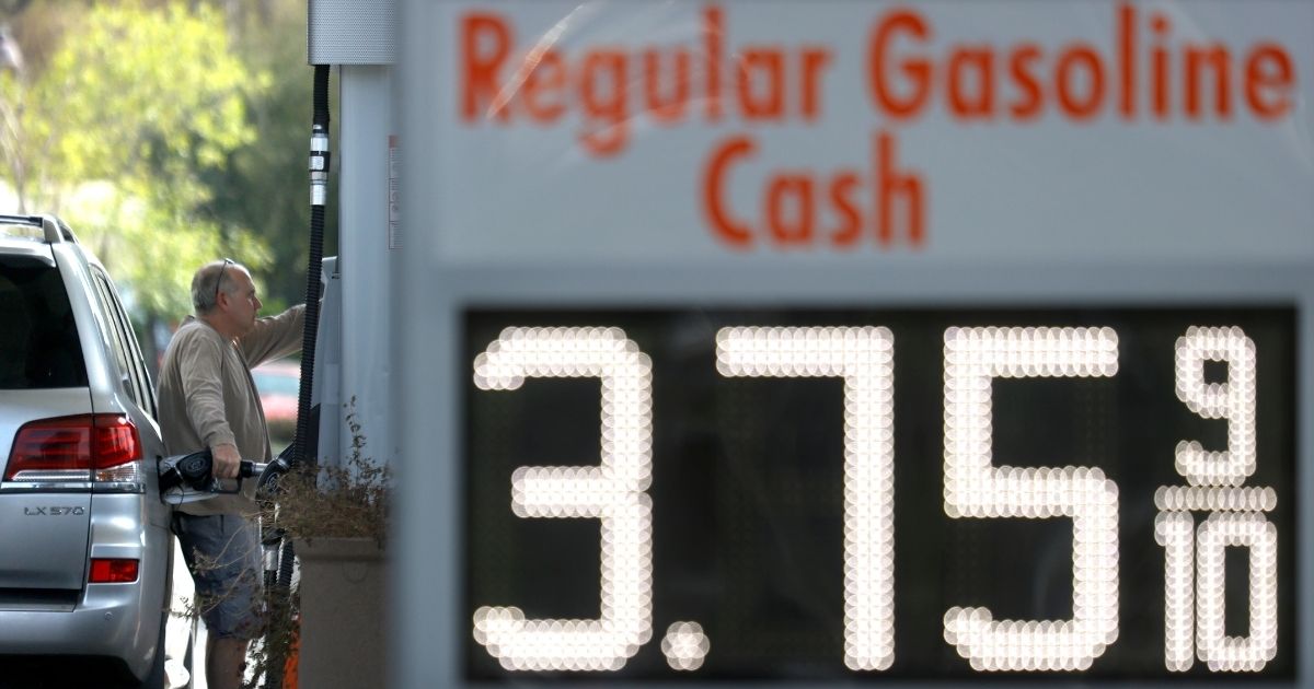 A sign showing regular gas at $3.75 per gallon is in the foreground as a man fills his tank at a 76 gas station in San Anselmo, California, on March 3.