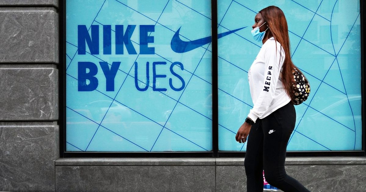 A woman wearing a protective mask and Nike attire walks by a Nike store on Aug. 25, 2020, in New York City.