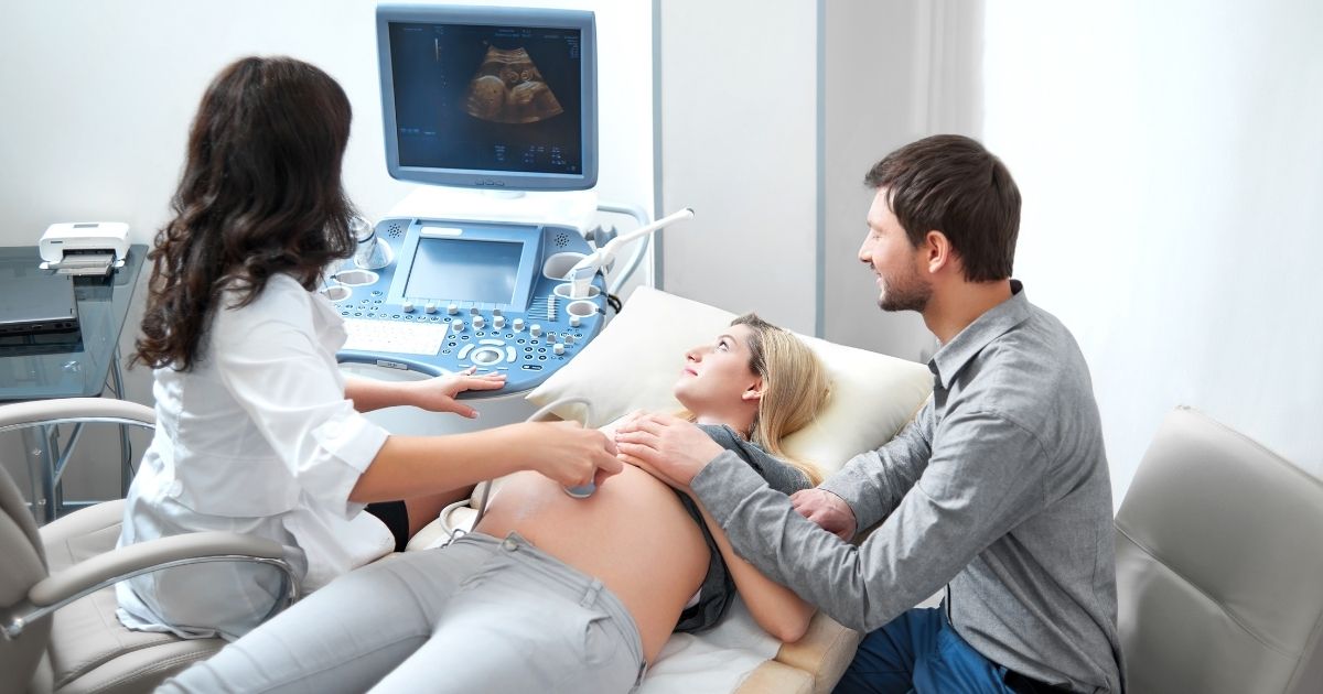 This stock photo portrays a couple at an appointment, as a doctor performs an ultrasound on the pregnant woman to examine the health of the baby.