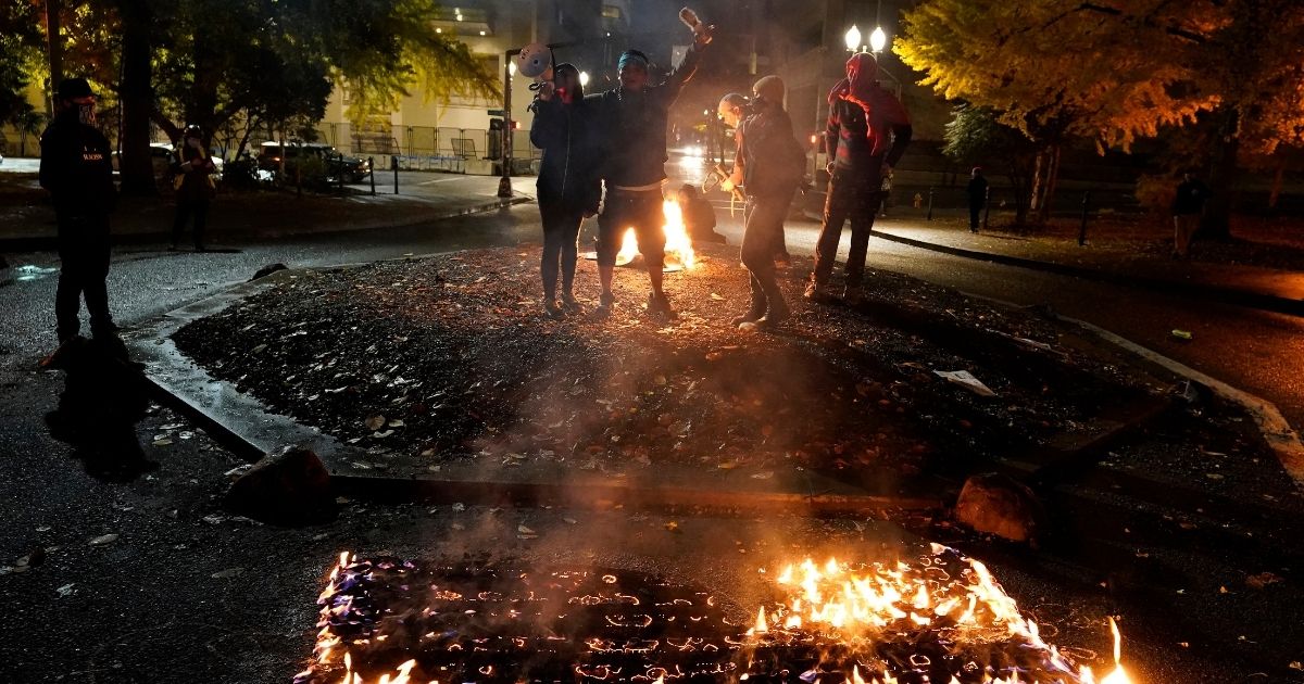 People watch as a flag burns outside of the Mark O. Hatfield United States Courthouse after a march on Nov. 3, 2020, in Portland, Oregon.