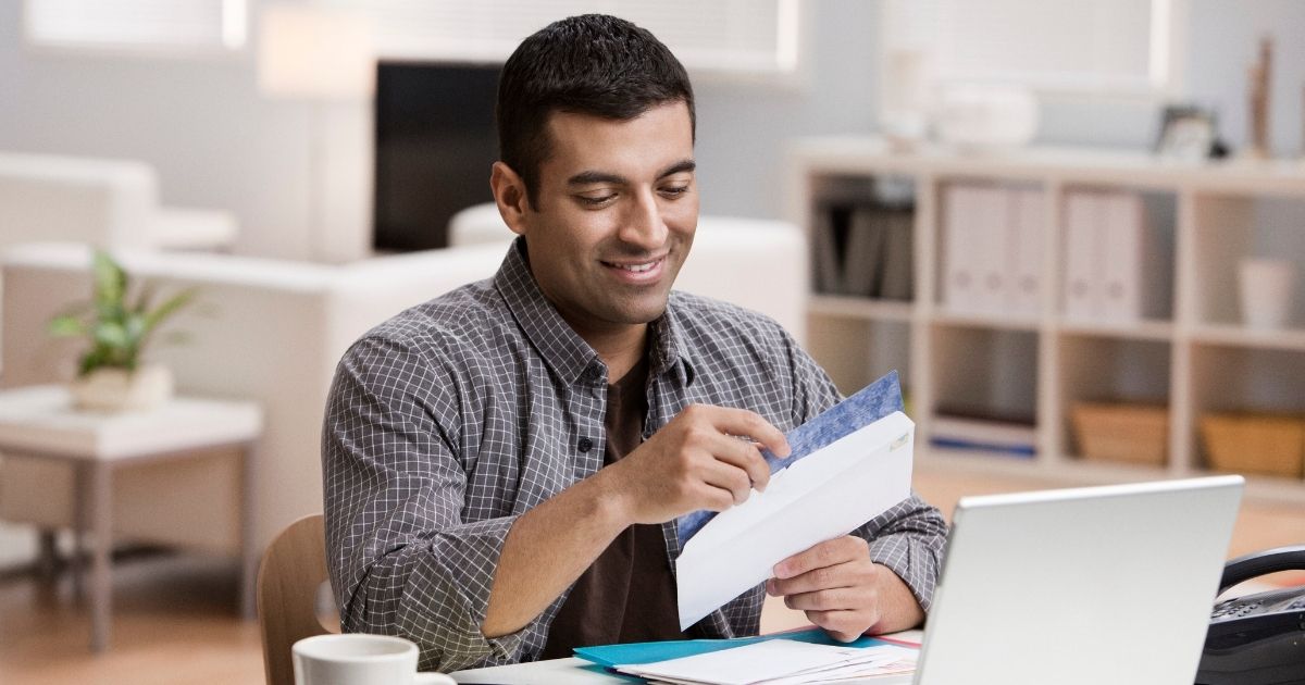 The above stock image shows a man opening the mail in his house.