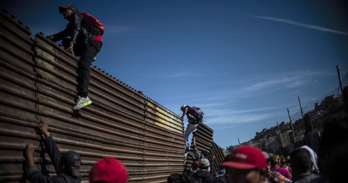 Migrants climb a metal wall on the border