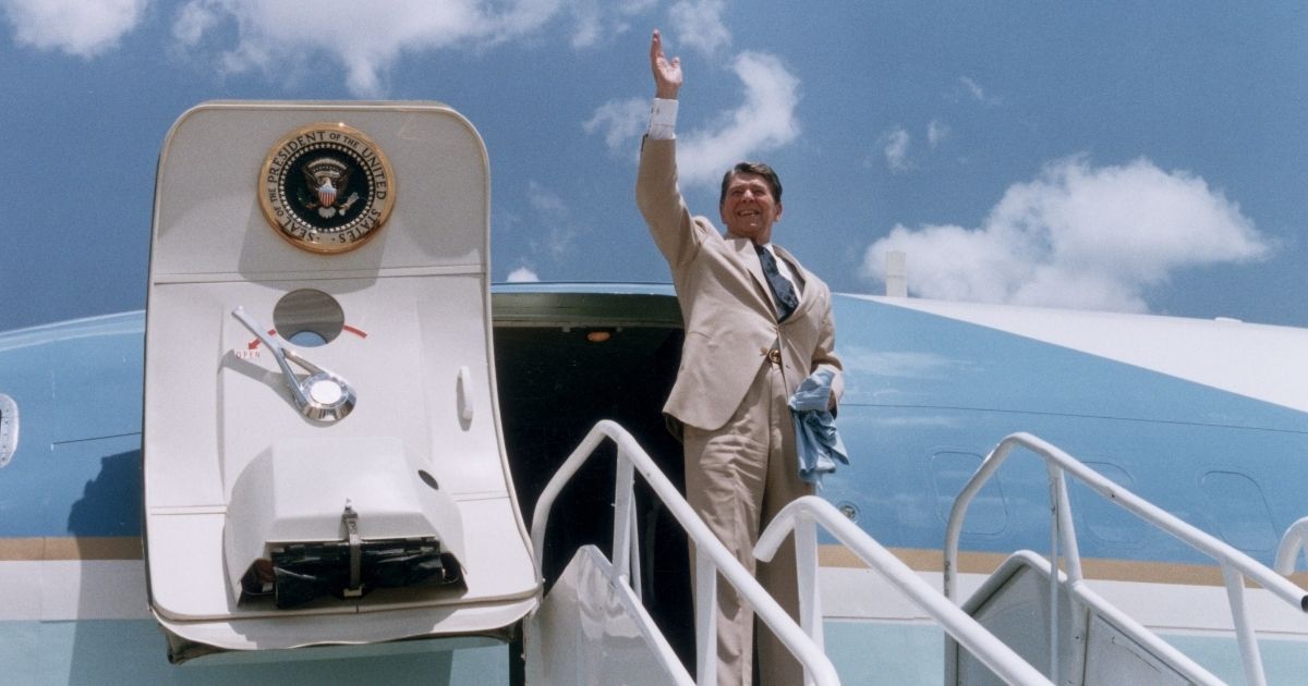Former President Ronald Reagan waves as he stands at the top of a stairway, preparing to board Air Force One in Dothan, Alabama.