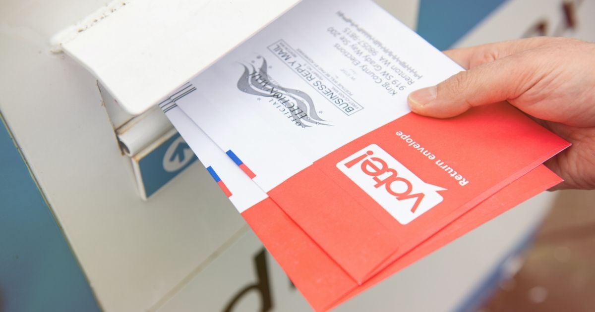 A woman drops off ballots in a mailbox in the above stock image.