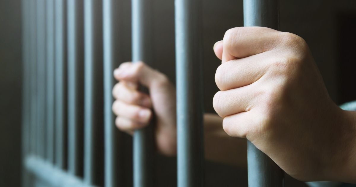 A man grips the bars of a prison cell in the above stock image.