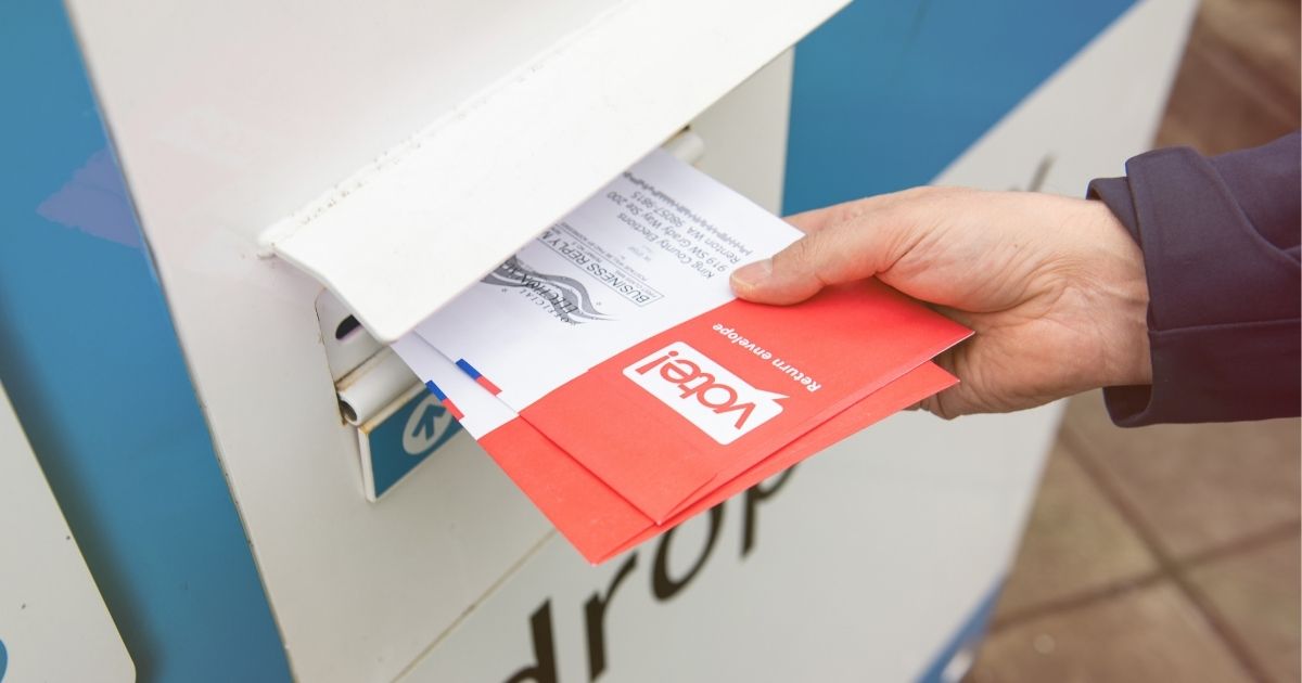 A man places a ballot in a drop box in the above stock image.
