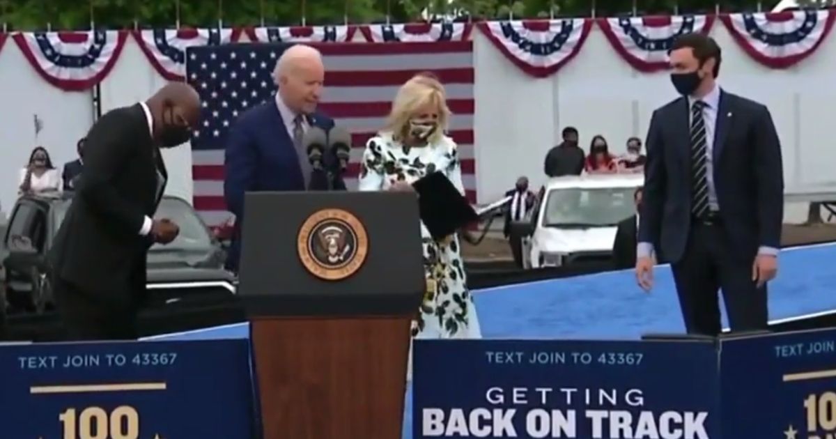 President Joe Biden, assisted by Democratic Sen. Raphael Warnock, left, and first lady Jill Biden, searches for his mask after delivering a speech in Georgia.