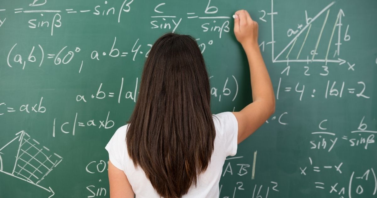 A student is pictured solving a math problem on a chalkboard in the stock image above.