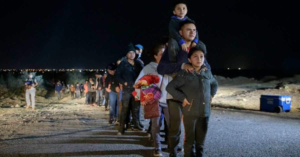 A family of immigrants who arrived illegally across the Rio Grande river from Mexico stand in line at a processing checkpoint on March 27, 2021, before being detained at a holding facility by border patrol agents in the border city of Roma.