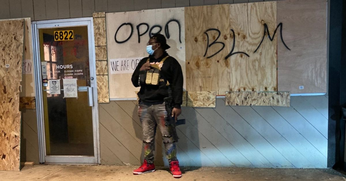 A Minnesota civilian stands guard outside a business as rioters loot stores on Monday night in Minneapolis, following the shooting of Daunte Wright.